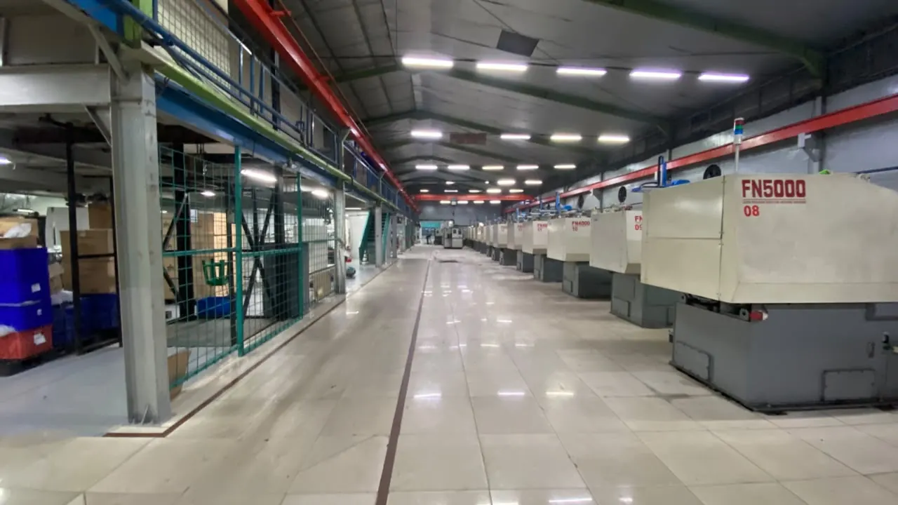 Lantai epoxy abu-abu mengkilap di lorong pabrik dengan deretan mesin injection molding