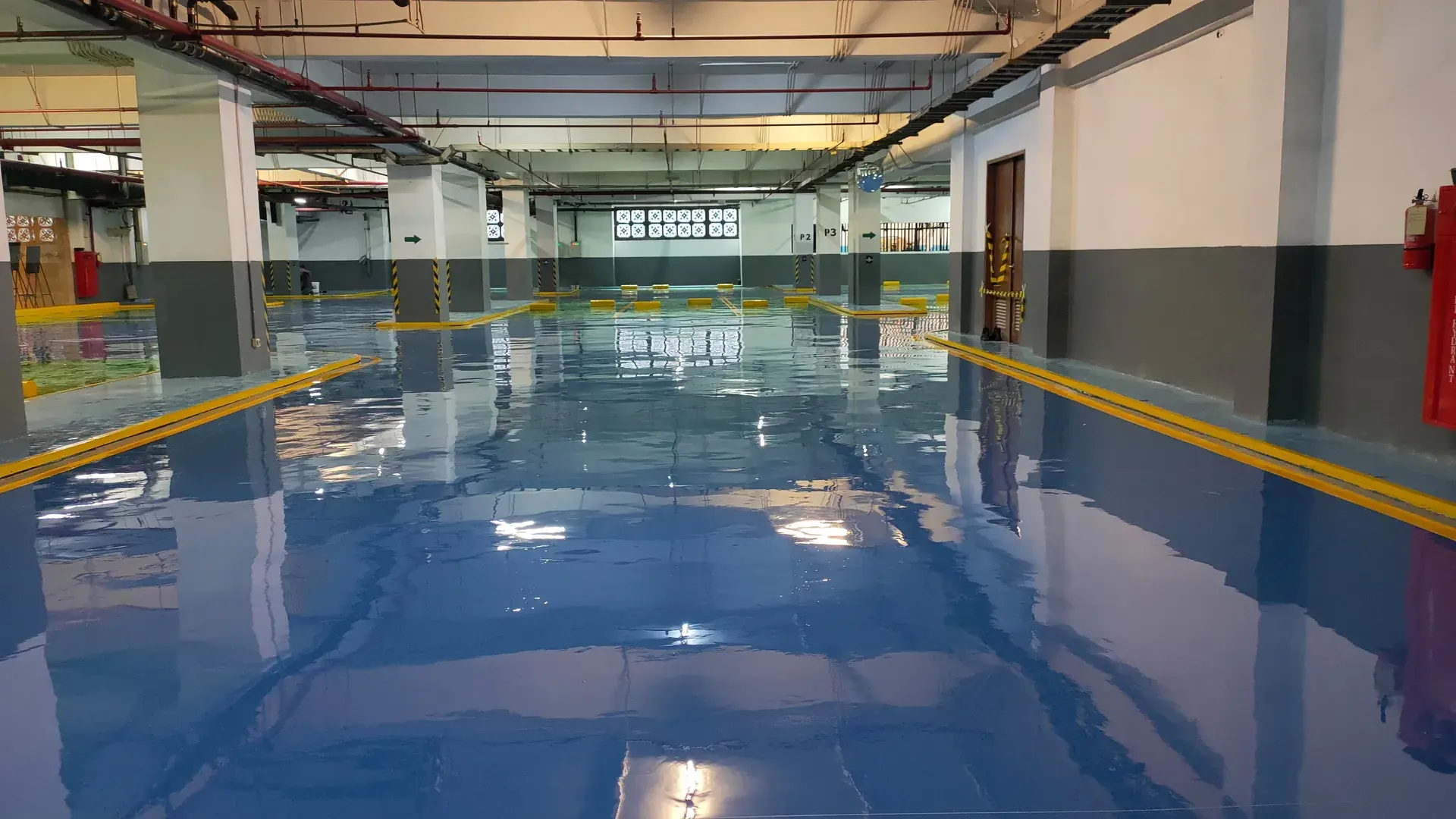 Lantai epoxy biru mengkilap di basement parkir dengan marka kuning