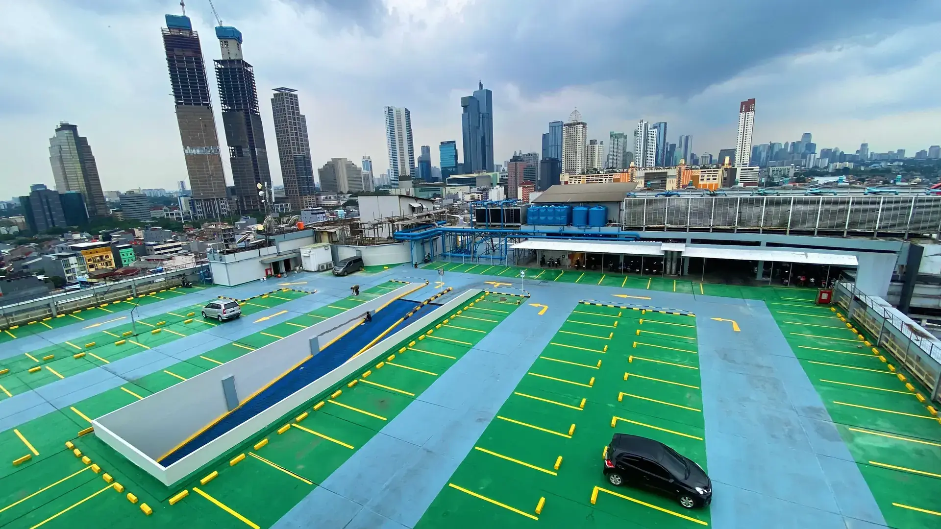 Lantai epoxy hijau dan biru di parkir rooftop gedung dengan latar gedung tinggi