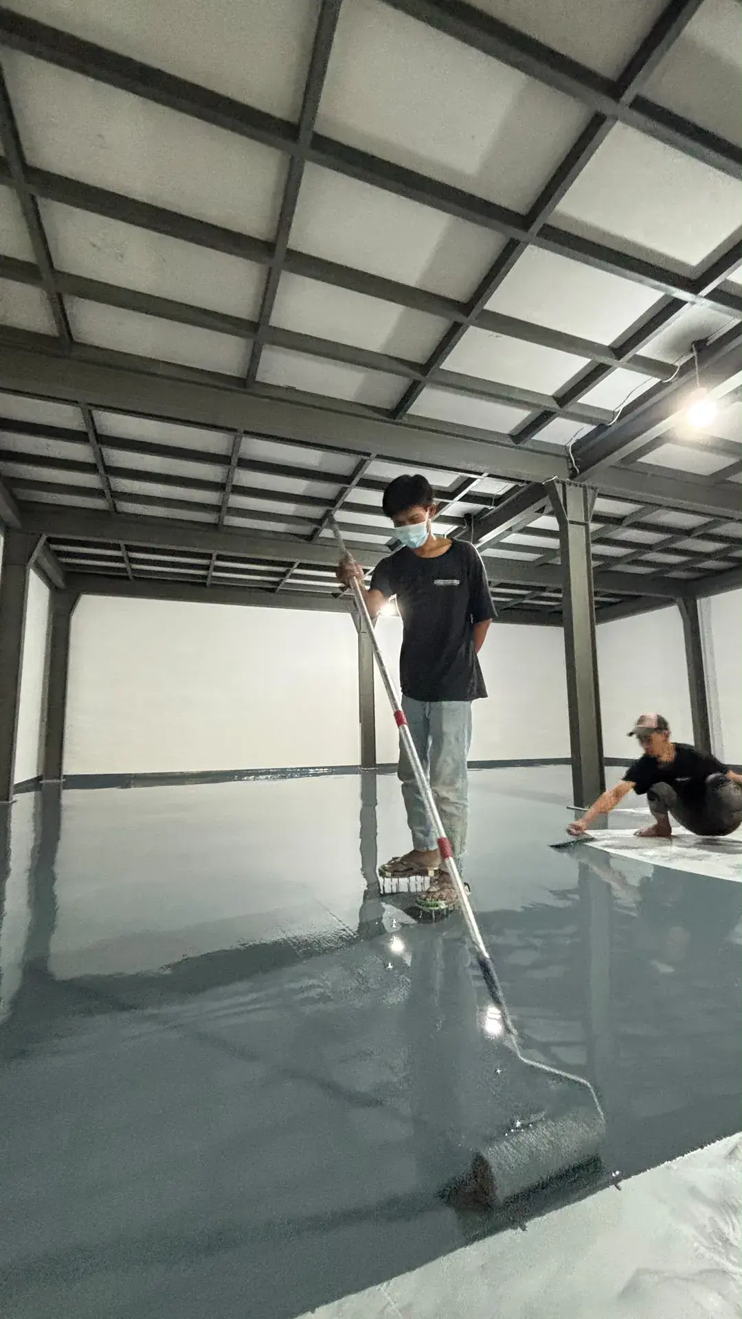Teknisi meratakan lapisan epoxy abu-abu dengan roller di gudang